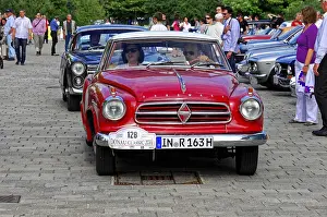 Red coupe vehicle at a vintage car event surrounded by people and other cars