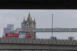Red double decker bus driving over a bridge with Tower bridge in the background