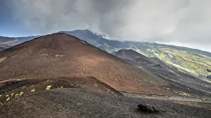 Red lava hill, cloudy sky, black crater