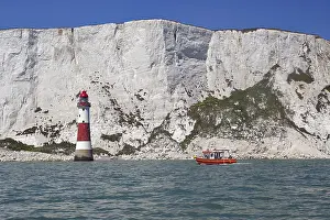 Red lighthouse and boat near white cliffs by the sea