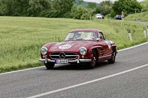 A red Mercedes classic car drives along a picturesque country road surrounded by trees