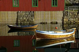 Red painted wooden house and rowboats reflected in the water