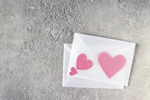 Red paper hearts inside transparent envelope on gray plaster