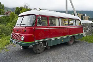 Red retro bus with green stripes on a road in a rural mountain landscape