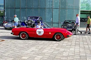 A red vintage convertible in front of a modern glass building at a car exhibition