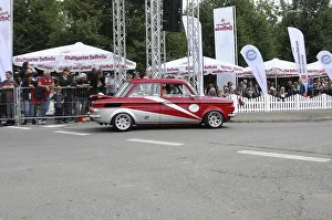 A red and white vintage car drives past enthusiastic spectators on a rally route