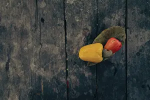 Red and yellow cashew fruits with a leaf on a textured aged wooden surface