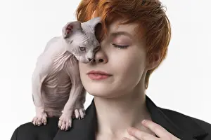 Redhead woman with closed eyes and playful kitten standing on shoulder
