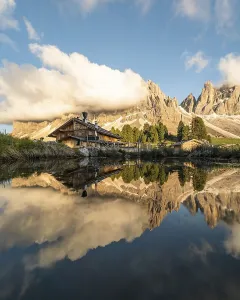 Reflection from the Furchetta mountain and the Geisler Alm hut in a pond near the Geisler Alm at sunset