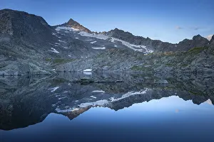 Reflection of snow-covered mountains on a calm water surface under a blue sky at sunrise