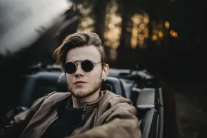Relaxed man in a convertible, wearing sunglasses as sun sets