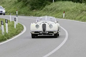 Retro white sports car driving on a winding country road through a green landscape under a blue sky