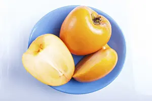 Ripe orange persimmon in a blue plate isolated on white background