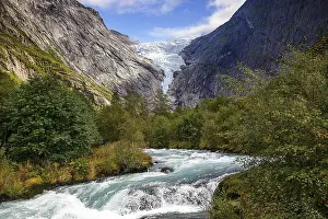 River flanked by mountains flows through a green valley with a view of the shimmering Briksdalsbreen glacier in Norway