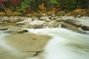 A river flows through a landscape with colourful autumn trees and stones on the banks