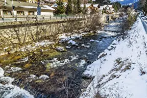 River passing through snowy alpine village in Italy illuminated by sun with mountains in the background