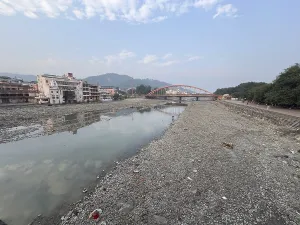 Empty riverbed with a bridge in the background and surrounding buildings under a cloudy sky