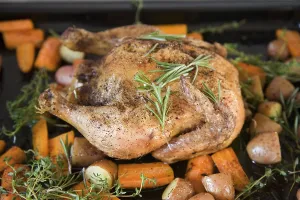 A roast chicken on a baking tray with rosemary