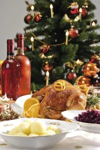 Roast turkey on a festive table setting served with red cabbage and dumplings in front of a decorated Christmas tree