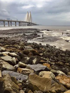 Rocks by the sea with a large bridge and urban background on a cloudy day