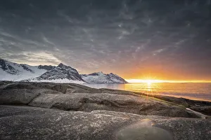 Rocky beach of Tungeneset, snow-covered mountain peaks in the warm sunlight above the sea