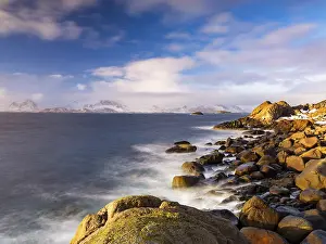 Rocky coast, snow-capped mountains in the background