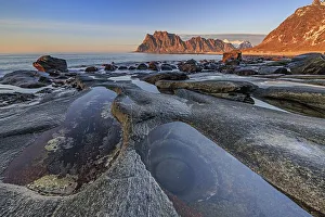 Rocky coast in front of steep mountains in the evening light
