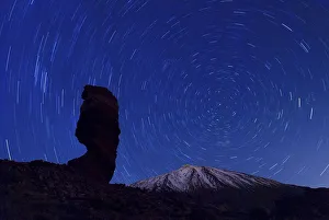 The Roque Cinchado at night with circling stars in the clear night sky and the summit of Pico de Teide