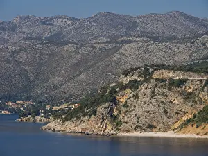 Rough coastline with large rocks and massive mountains behind them on the clear sea