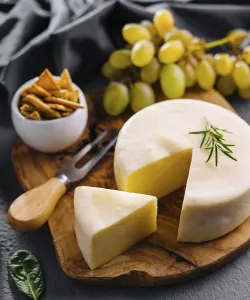 Round cheese on a wooden board and green grapes