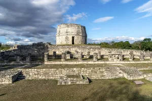 Round stone tower in archaeological site with Mayan ruins and cloudy sky