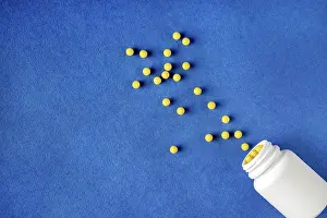 Round yellow vitamins spilled out of a white jar on a blue background