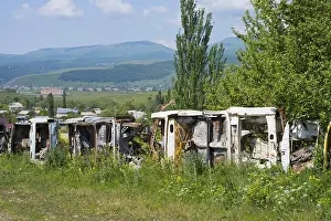 Row of rusty cars in a meadow with green trees and mountains