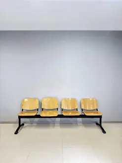 A row of four wooden chairs with metal frames placed against a light gray wall