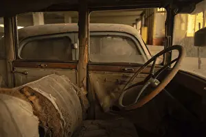 Rusted classic car interior with torn upholstery and wooden steering wheel in an abandoned garage
