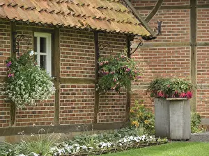A rustic half-timbered house with hanging baskets and lush vegetation