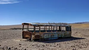 A rusty bus stands in a lonely desert landscape under a clear blue sky