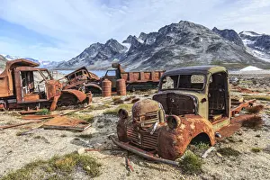 Rusty cars and oil drums in front of steep mountains