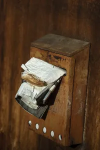 A rusty mailbox attached to a weathered wall is bursting with various papers and ads