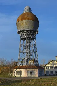 A rusty water tower with industrial construction on a meadow