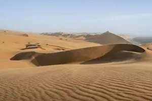 Sand dunes with wave patterns and sea in evening light