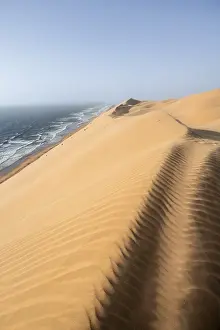 Sand dunes with wave patterns and sea in evening light