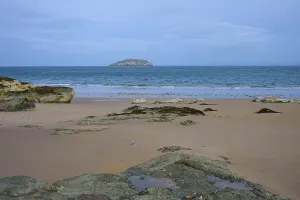 Sandy beach beach with rocks and distant island under cloudy sky