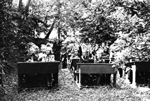 School class sits on wooden benches in the open air