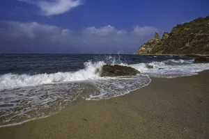 Sea crashing against rocks on the beach under a clear blue sky