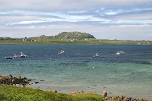 Sea view with several boats and a rocky coastline under a slightly cloudy sky