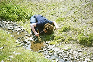 Secondary school student doing geographical fieldwork, Great Britain 1970s: Girl measuring the depth of a small stream with a ruler, 1977