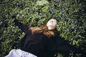 A serene teenage girl lies on a bed of lush periwinkle flowers