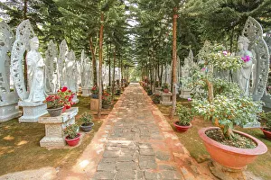 Serene walkway surrounded by trees and Buddhist sculptures illuminated by sunlight