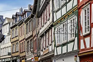 Framed Print : A series of half-timbered houses in various colors that form a lively street scene